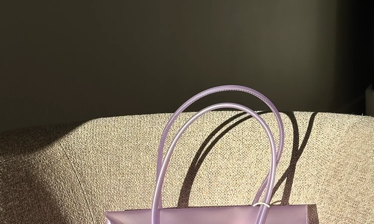 top of a frosted light purple jelly tote on a linen armchair, with two rolled lilac handles