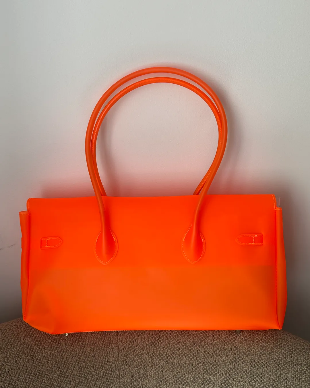 translucent neon orange East West bag seen from the back, with long rolled orange handles